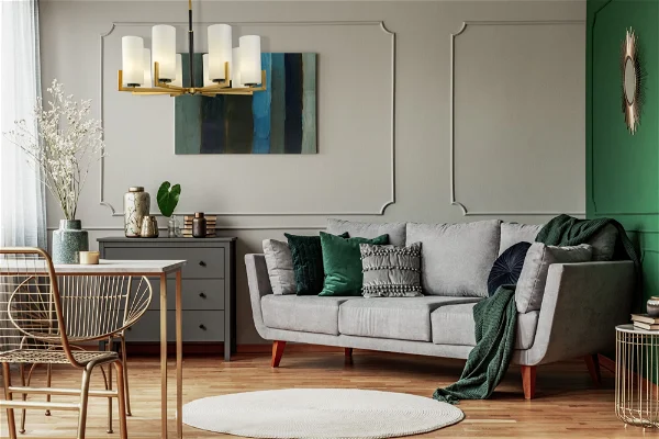 A living area with a gray couch and a combination of green pillows with a hanging chandelier