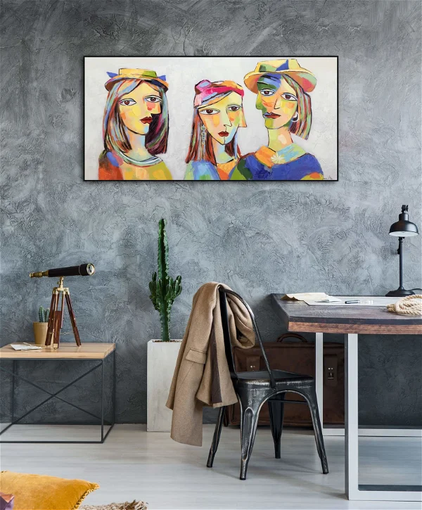 Wide contemporary painting featuring three abstract women with expressive eyes and vibrant colors, hung on a textured gray wall in a modern office space with industrial decor elements.